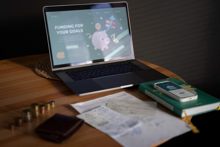 Ordinateur portable affichant une page de finance en ligne avec tirelire et documents financiers sur un bureau en bois